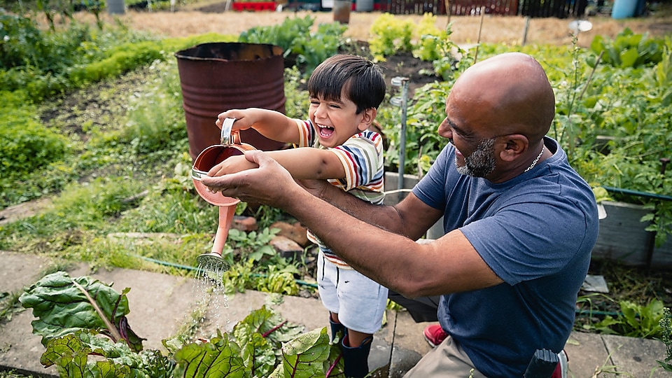 Hombre ayudando a un niño sonriente a regar plantas en un jardín