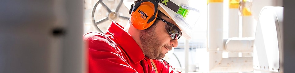 Hombre trabajando en una planta industrial usando un casco y audífonos.