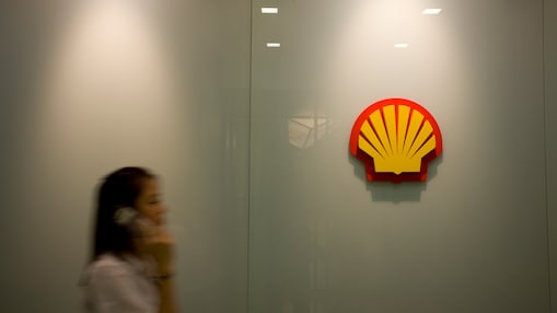 Mujer habla en teléfono móvil con la marca Shell al fondo