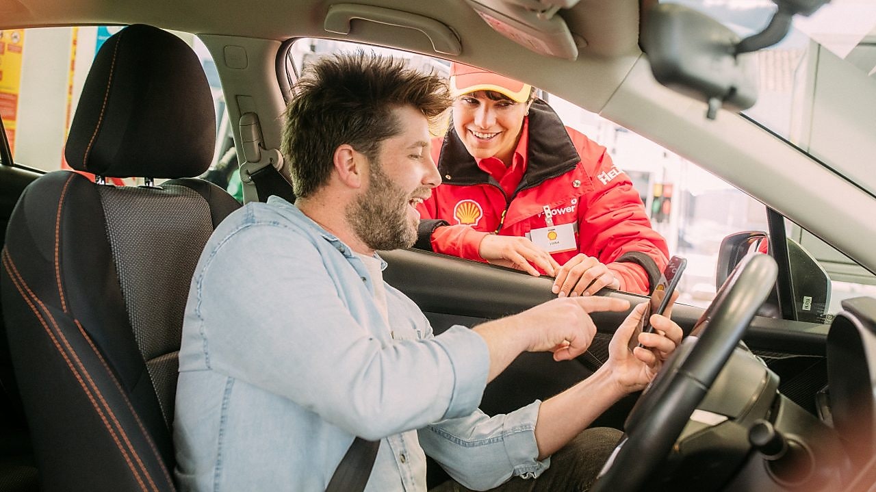 Un hombre en su auto, conversando con una atendedora mujer en la estación de servicios