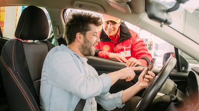 Un hombre en su auto, conversando con una atendedora mujer en la estación de servicios