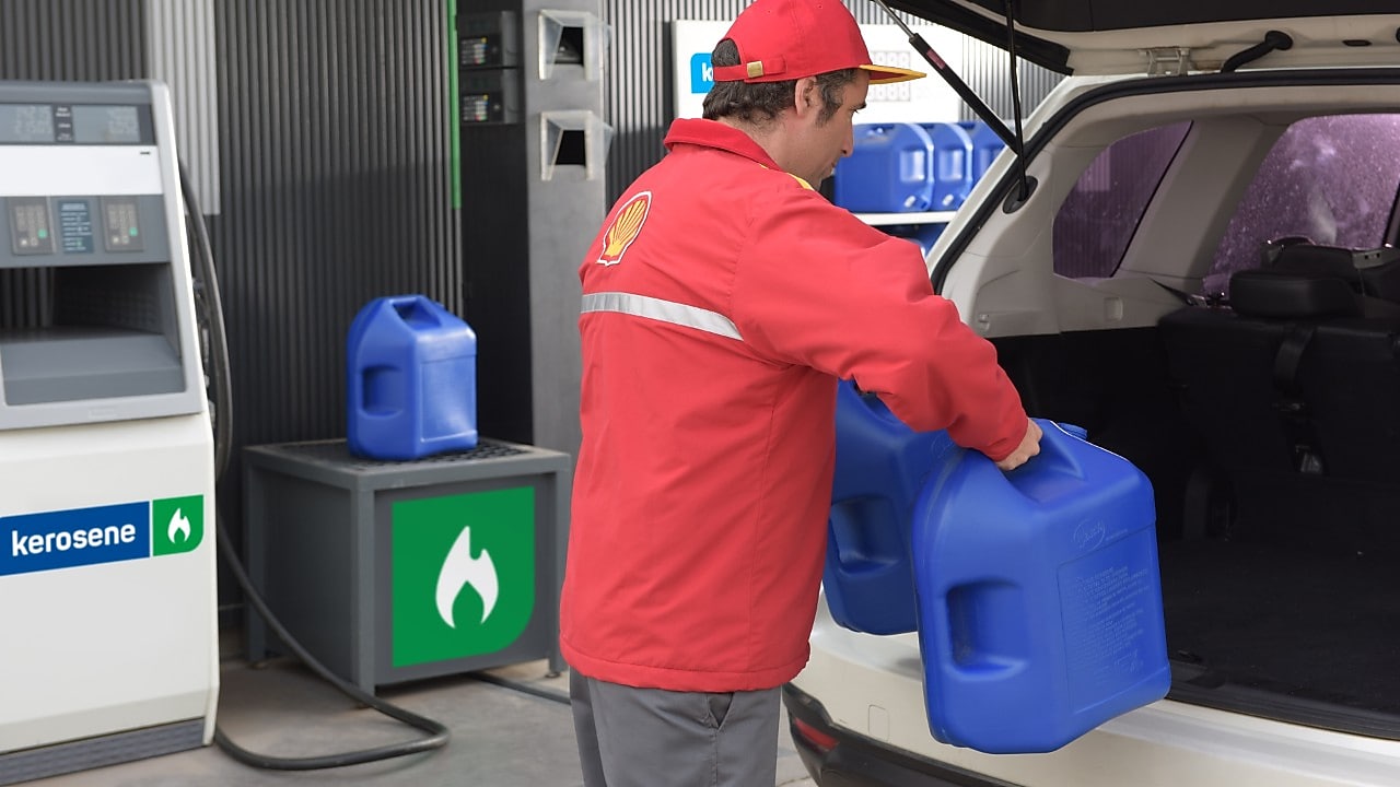 Un atendedor de estación de servicios Shell cargando dos bidones de kerosene en el portamaletas de un auto.