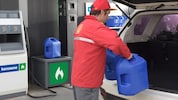 Un atendedor de estación de servicios Shell cargando dos bidones de kerosene en el portamaletas de un auto.